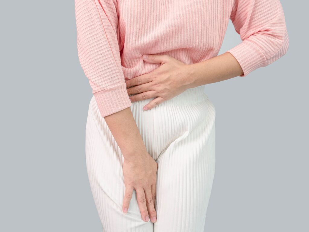 woman wearing white pants and a pink sweater holding her stomach and pelvic area indicating she is having her period
