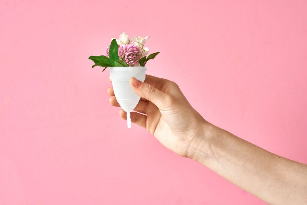 hand holding a menstrual cup with flowers in it, against a pink background