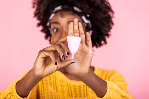 African American woman in yellow sweater holding up a white menstrual cup