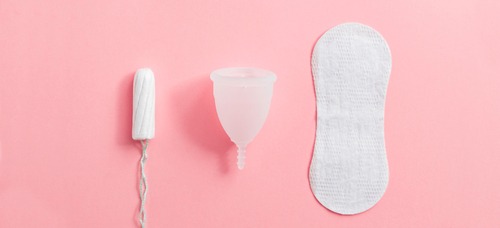a tampon, a white menstrual cup and a sanitary pad against a light pink background