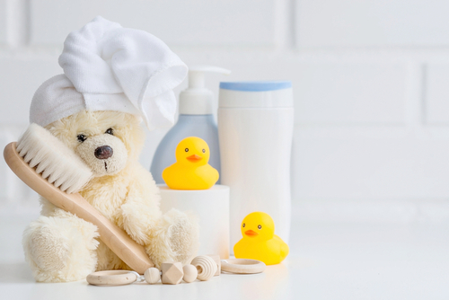 a white bathroom shelf with a teddy bear with a white towel wrapped on its head, yellow rubber ducks and white bottles of bathroom supplies