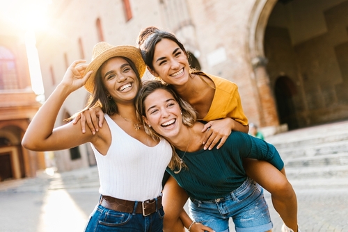 3 young brunette women smiling on vacation outside an old brick European building