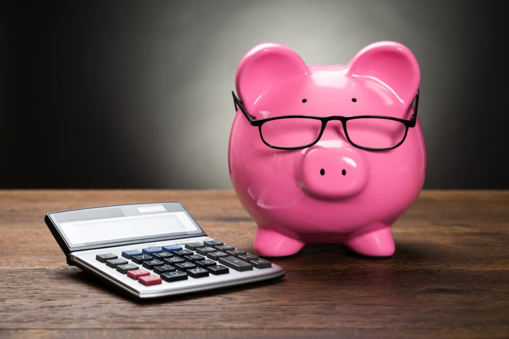 a wooden desk with a bright pink piggy bank wearing glasses and a large calculator on top of t