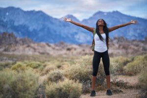 young woman stood in the wilderness and mountains with her arms stretched out enjoying herself