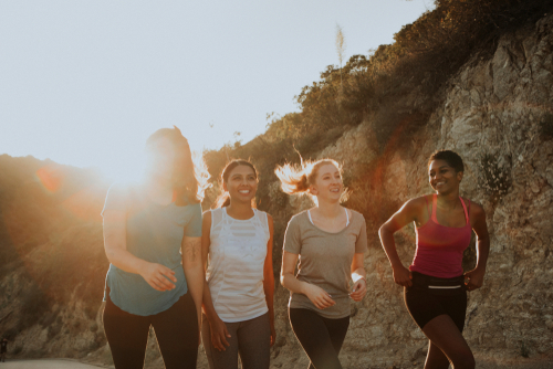group of 4 young women smiling and hiking in casual and yoga wear with a sun setting in the background