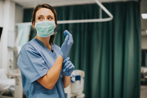 woman in scrubs and surgical mask putting on latex gloves in a hospital