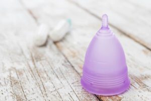 a light purple menstrual cup and two tampons on a wooden table