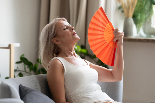 Middle Aged woman sitting back on couch fanning herself with orange fan