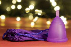 purple menstrual cup on a wooden table next to a purple pouch