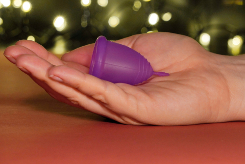 side close up of a hand with a small purple menstrual cup