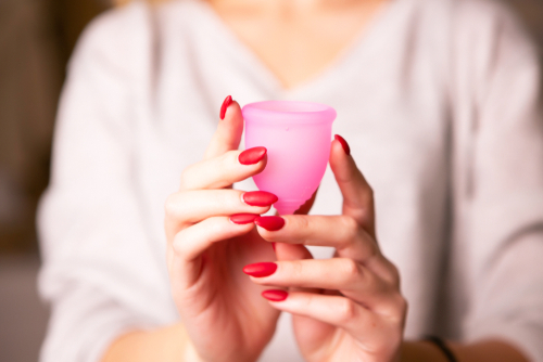 close up of woman hands with red nail polish holding a pink menstrual cup in front of her