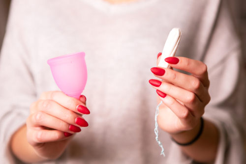 close up on woman hands holding a pink menstrual cup in one hand and a tampon in the other