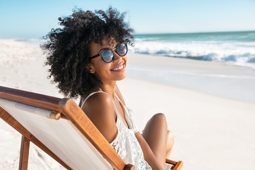 young woman with afro hair looking back from deckchair on beach smiling with ocean in background