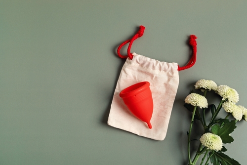 a red menstrual cup on a cream pouch with red ties, against a green background