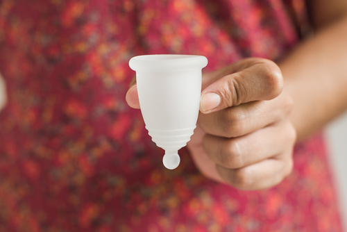 close up of a woman hand holing a white menstrual cup with her red patterned blouse in the background