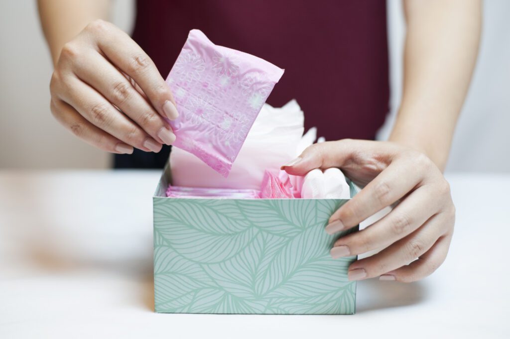 close up of small box with pink wrapped sanitary towels on a table and a woman's hands taking one out
