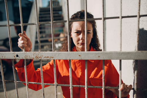 woman prisoner in orange jumpsuit standing behind bars