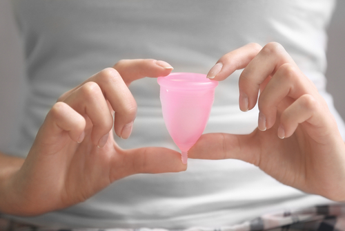 close up of a woman hands holding a menstrual cup between her fingers against background of her white shirt